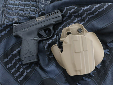 Black handgun with beige holster on a textured surface