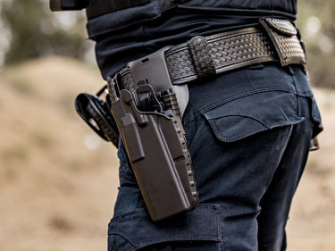 Person wearing tactical pants with a gun holster on a blurred natural background