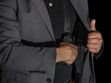 Person holstering a weapon in a gray suit against a black background
