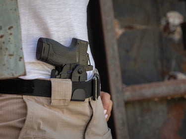 Person wearing a black gun holster on a belt with a blurred background