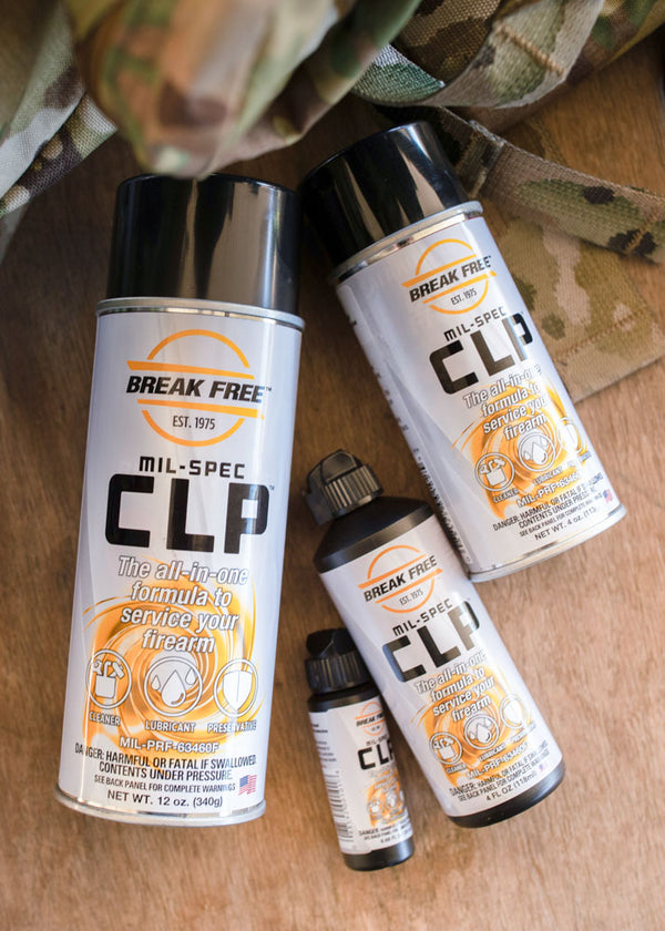 Three cans of Break Free Mil-Spec CLP on a wooden surface with camouflage fabric.